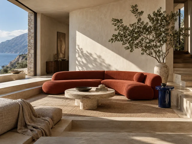 A sunken cream conversation pit, sculptural vermilion sofa, and cobalt side table in a sunlit plaster interior.
